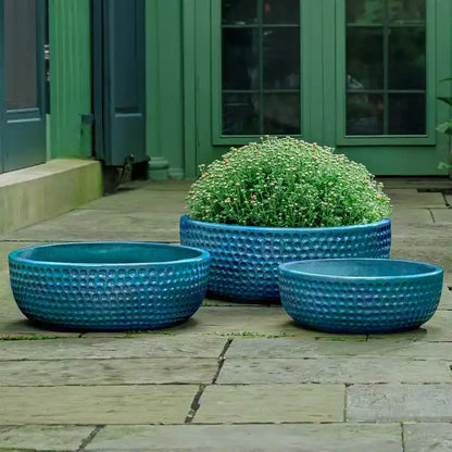 Three blue textured planters on a wooden deck with a green building in the background.