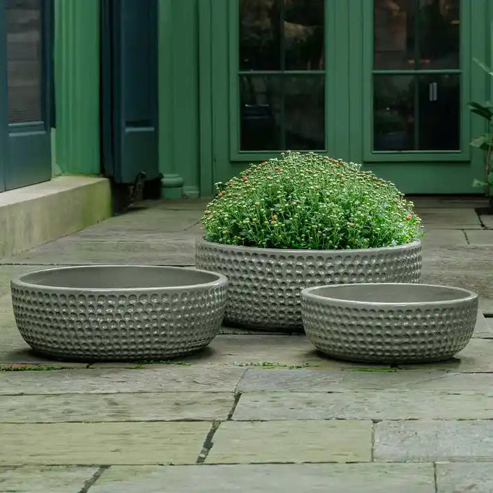 Three textured stone planters with green plants on a wooden deck.