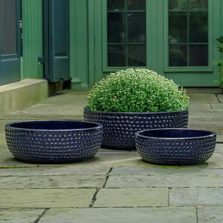 Three dark blue textured planters on a wooden deck with a green door in the background.