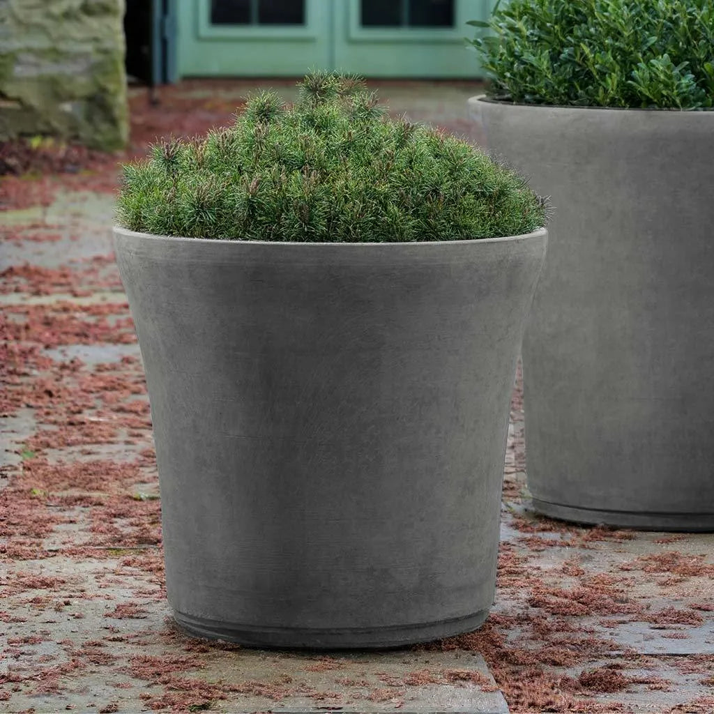 Evergreen shrub in large gray SkinnyCrete cloche planter on a stone garden terrace